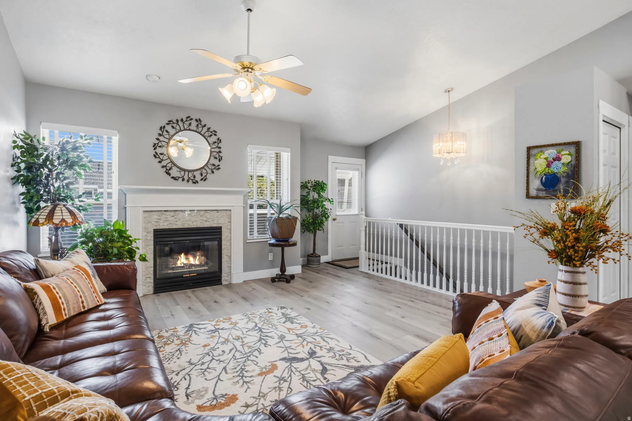 Wood-finish flooring, white-painted fireplace mantel, tiled fireplace surround, ceiling fan with integrated lighting, and a crystal chandelier
