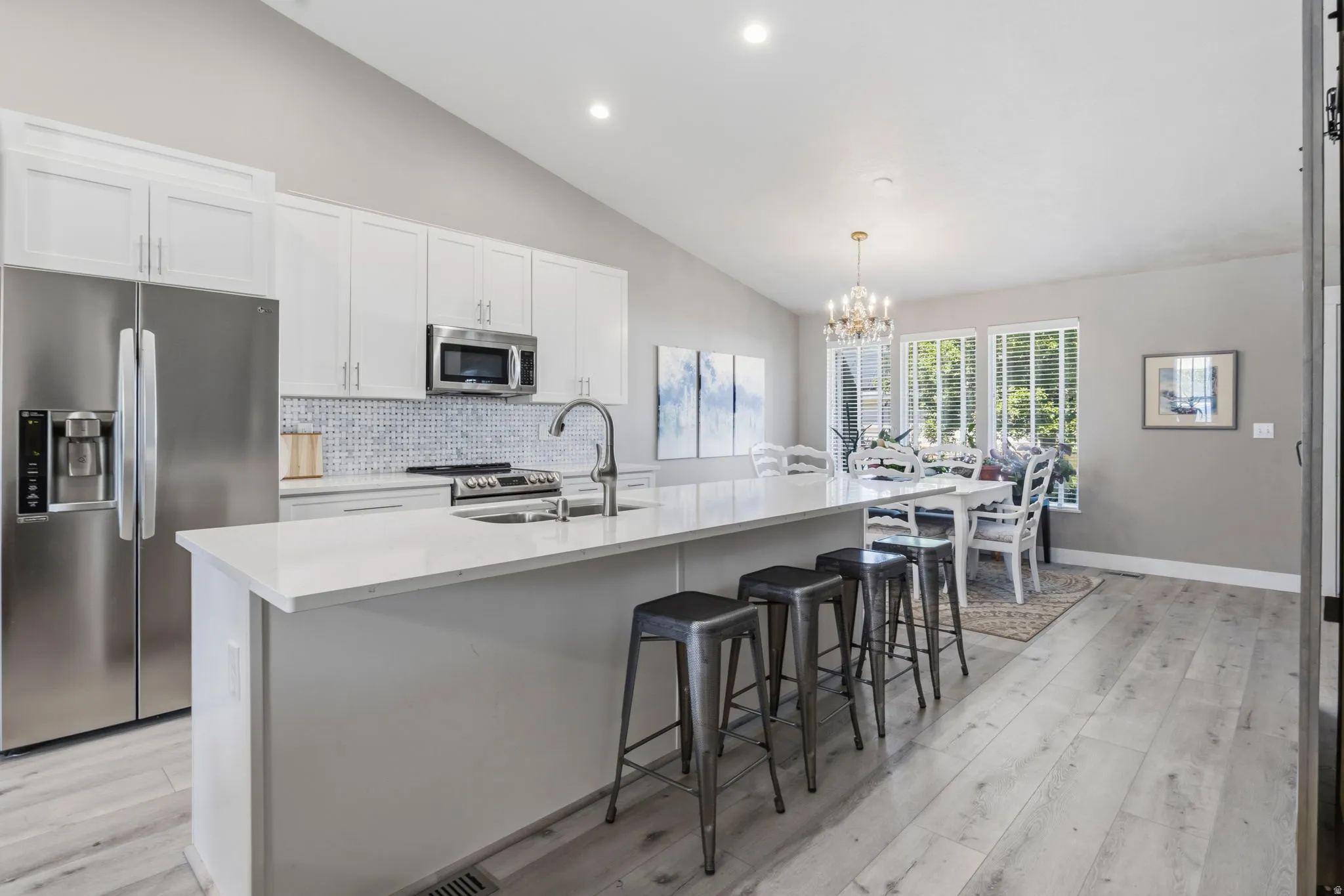 Contemporary kitchen featuring white cabinetry, stainless steel appliances, a white tile backsplash, and light wood-finish flooring