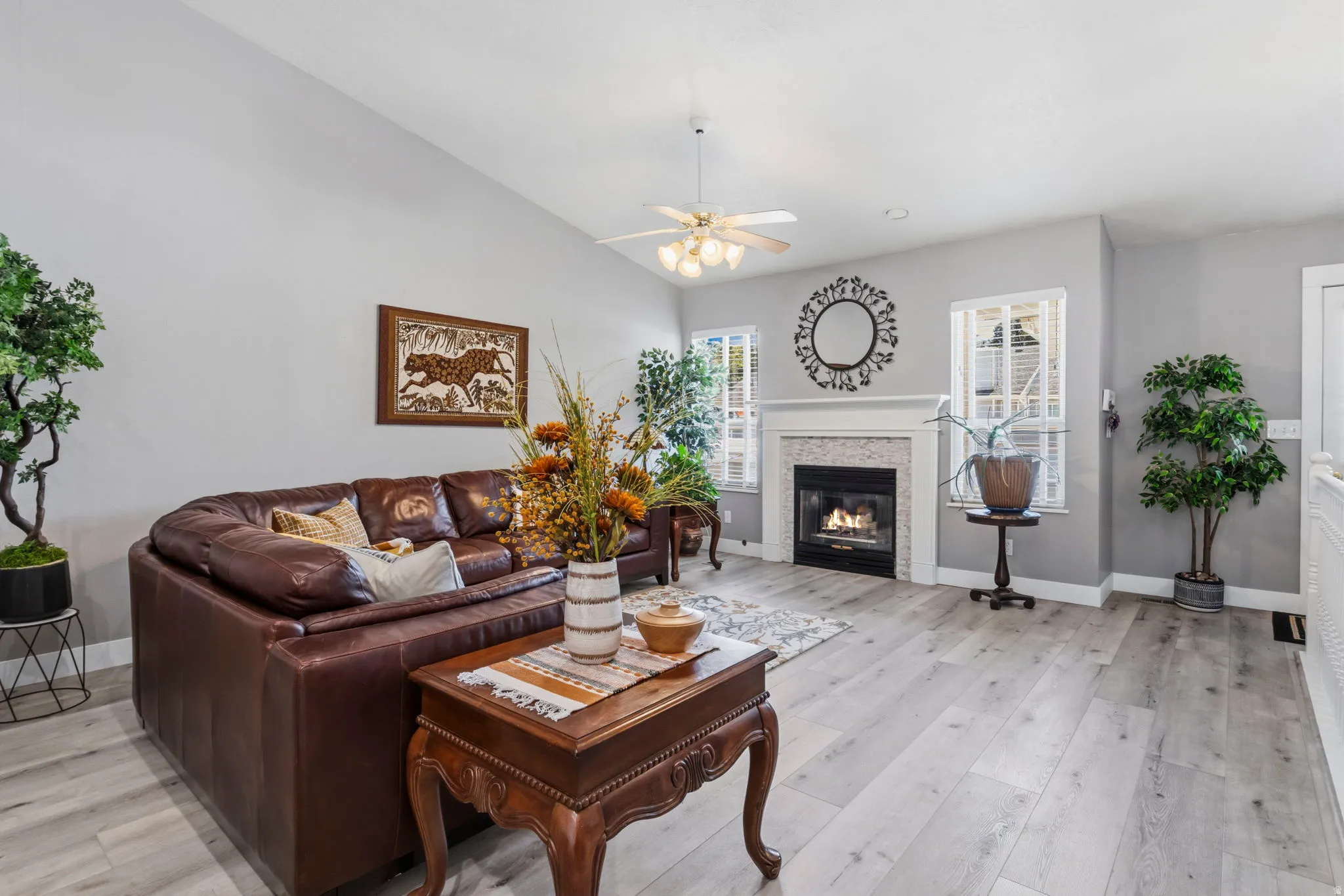 Vaulted ceiling, wood-finish flooring, white trim, recessed fireplace with tile surround, and an overhead ceiling fan