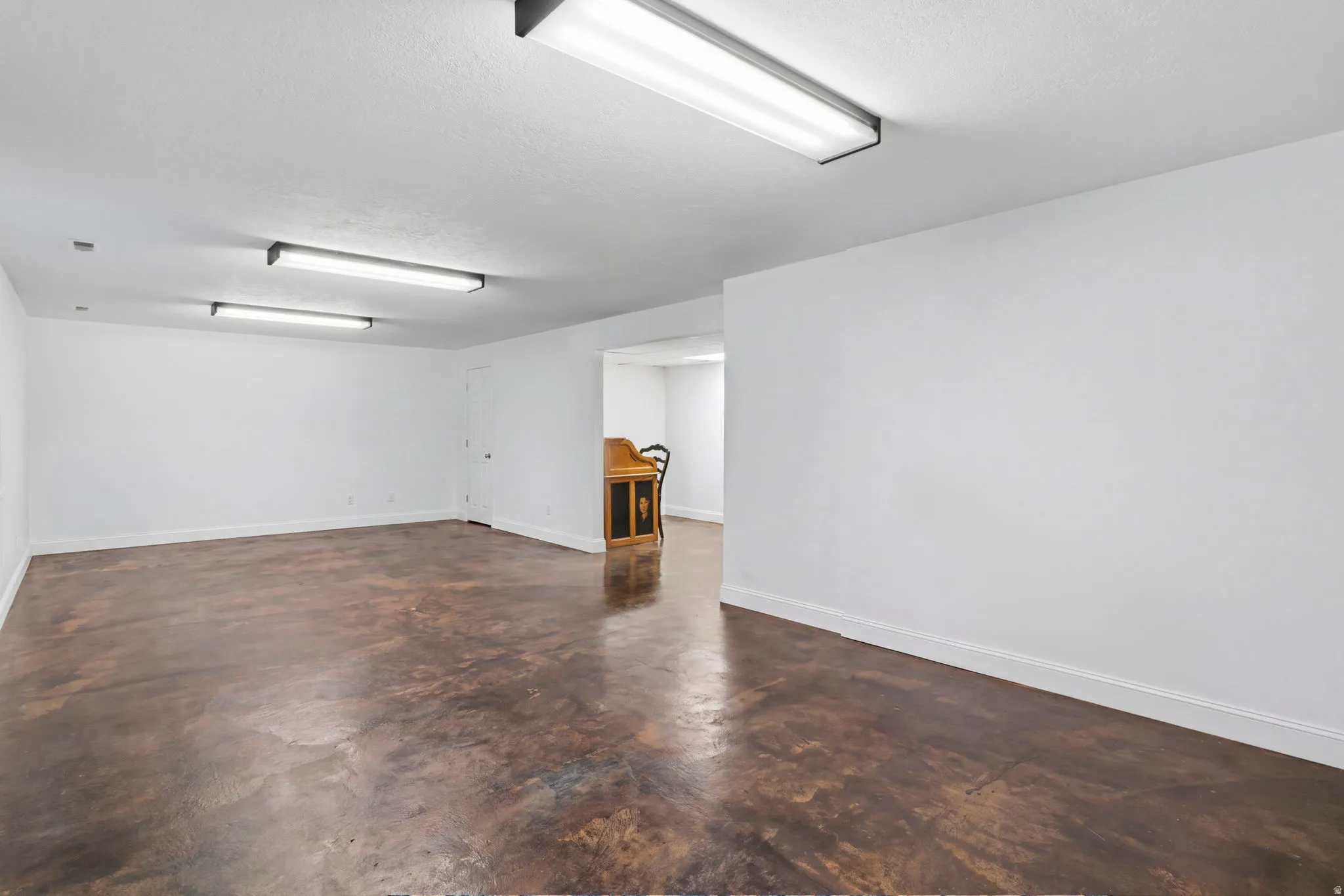 Expansive room featuring stained concrete flooring, bright overhead lighting, and white painted walls