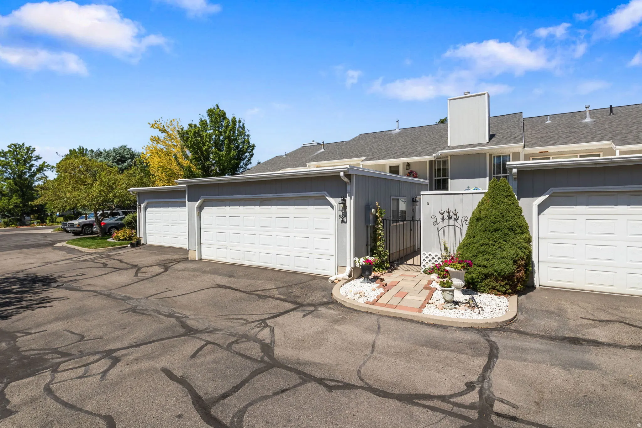 Attached single-car garages, grey siding exterior, paver walkway, and a decorative metal gate