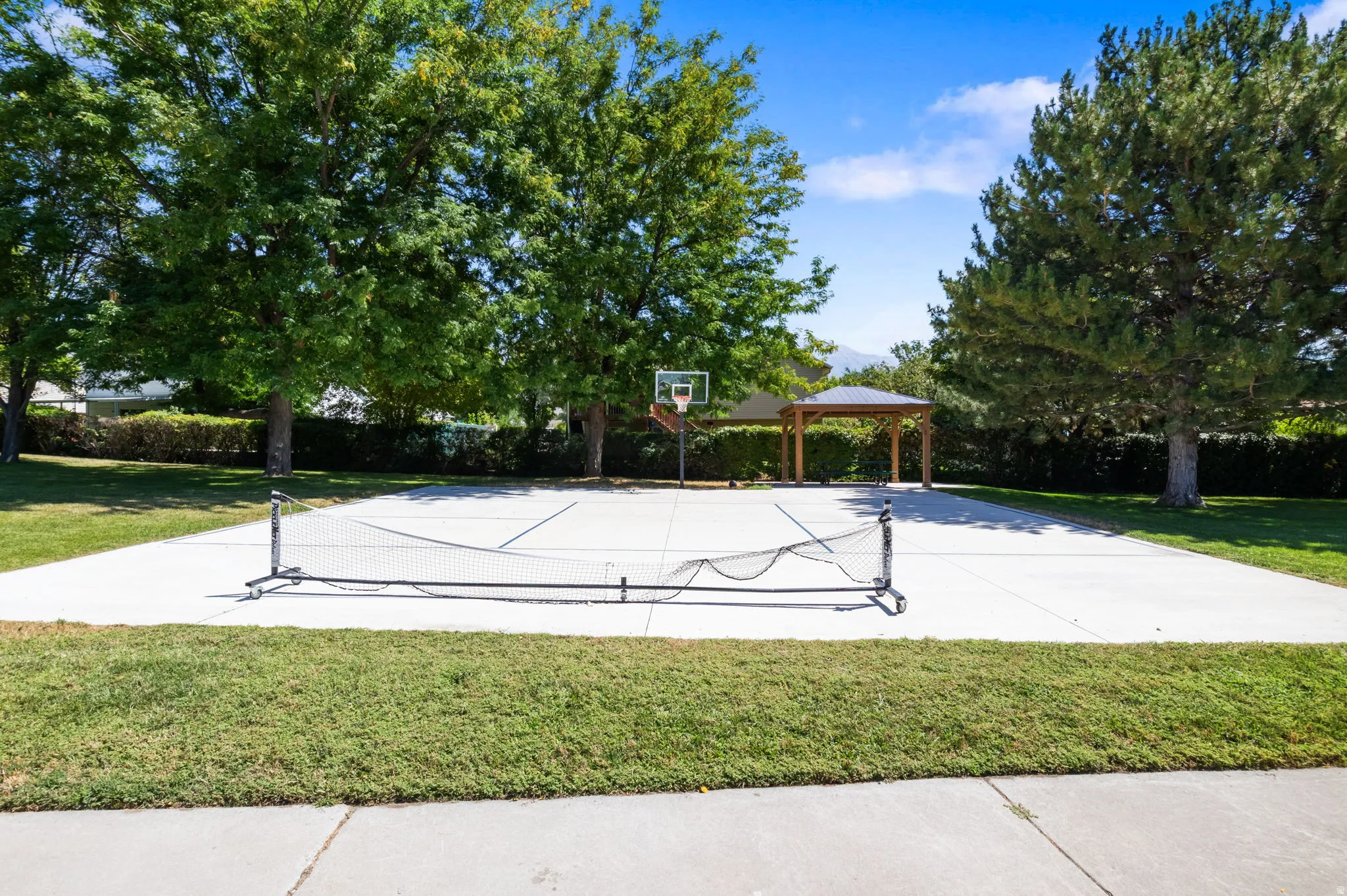 Expansive recreational court with a basketball hoop and a detached wooden gazebo