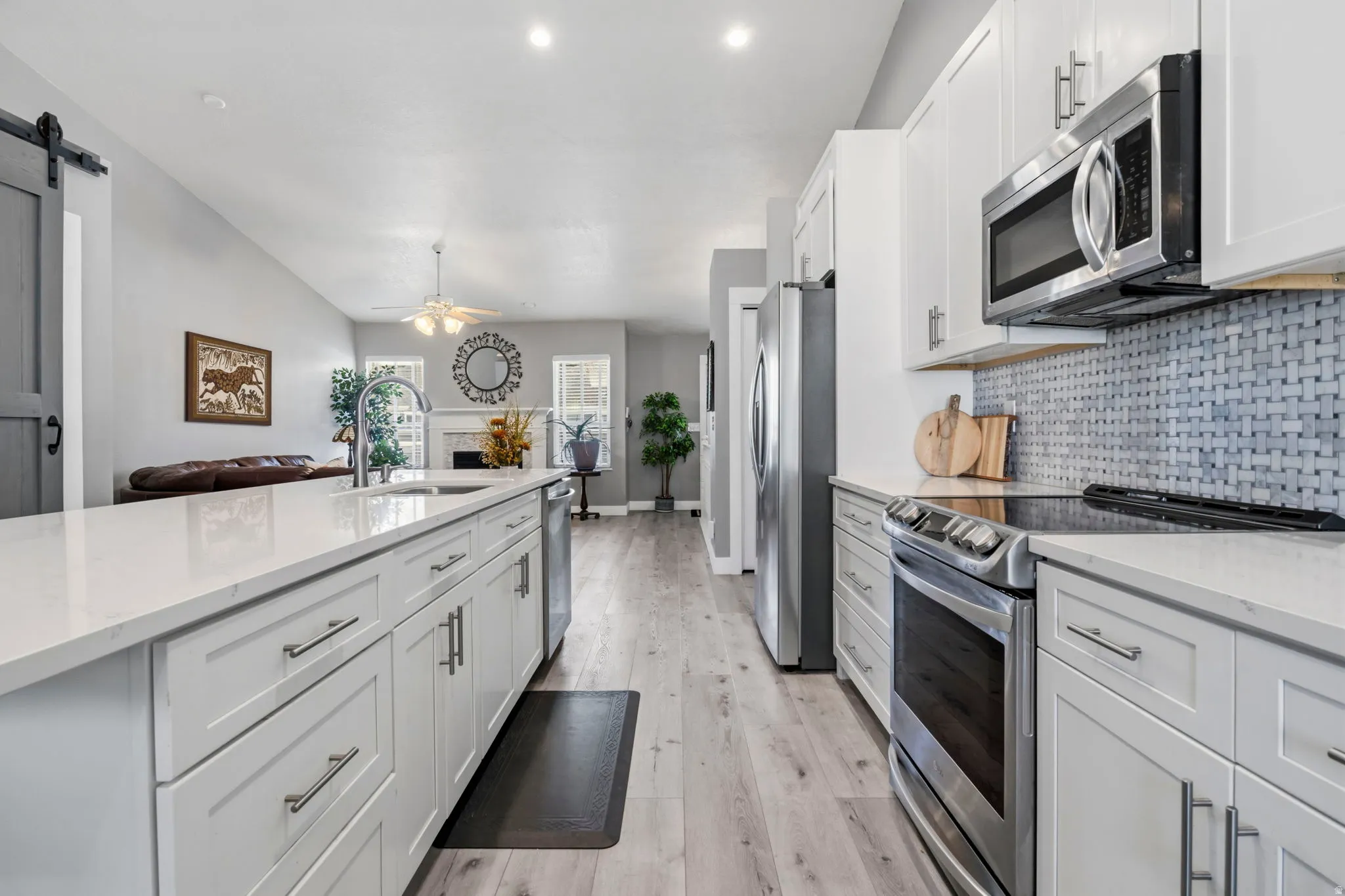 Modern kitchen with stainless steel appliances, white cabinetry, a tile backsplash, and light wood-finish flooring