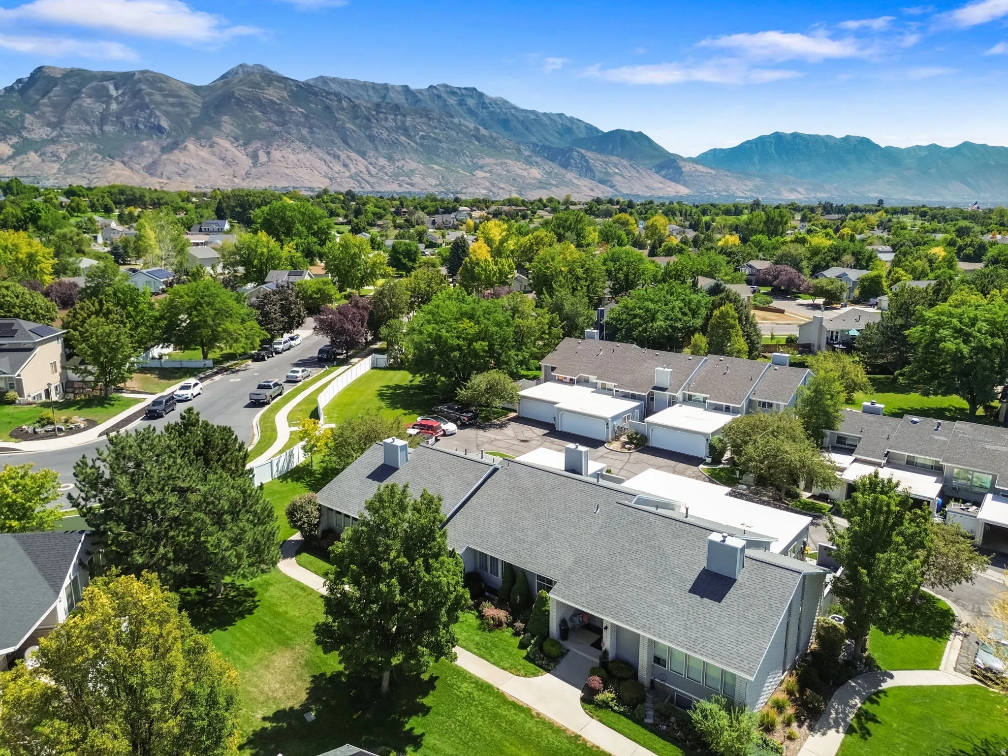 Residential community with mountain backdrop, mature trees, and a paved street