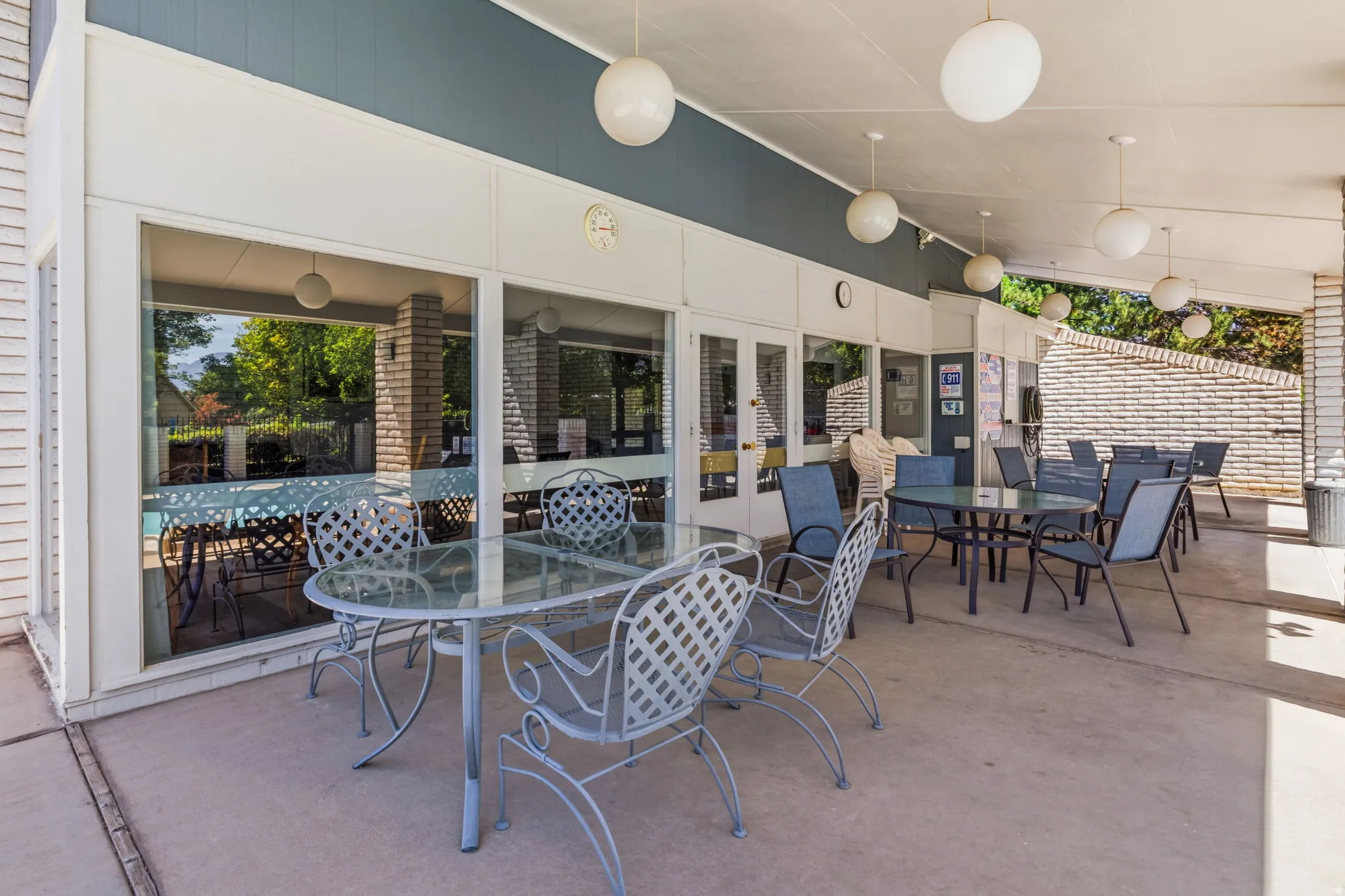Covered patio area between Clubhouse and Pool featuring concrete flooring, multiple globe pendant lights, and a brick accent wall
