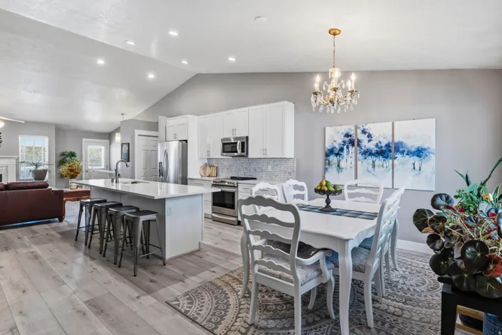 Vaulted ceiling with recessed lighting, wood-finish flooring, white cabinetry, stainless steel appliances, and a kitchen island with seating