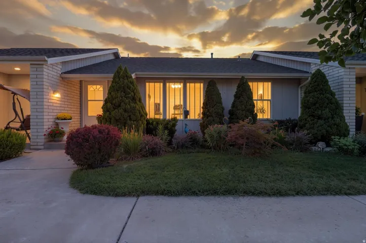 Single-story residence featuring a covered entry porch, white brick exterior accents, a well-maintained lawn, and established landscaping