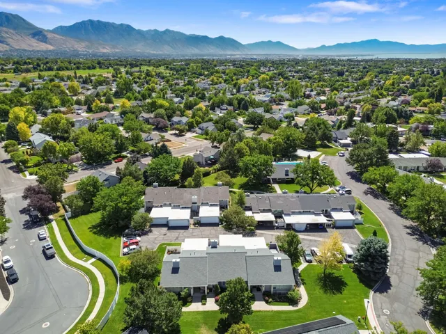 Residential community featuring mature trees, landscaped green spaces, paved streets, and mountain ranges in the distance