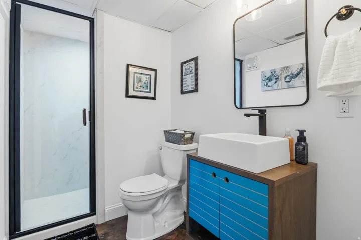 Walk-in shower with clear glass enclosure, modern vanity with vessel sink, matte black wall-mounted faucet, and rectangular framed mirror