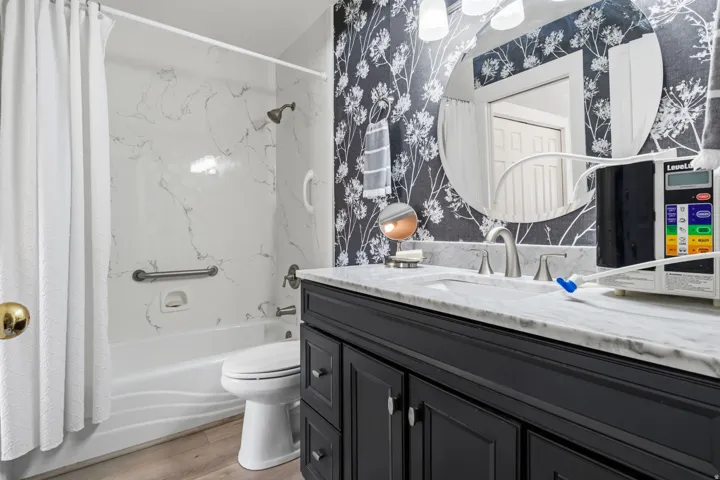 Tub/shower combination with a marble-patterned surround, dark-finish vanity with a light-tone countertop, and Gray LVP flooring