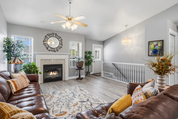 Wood-finish flooring, white-painted fireplace mantel, tiled fireplace surround, ceiling fan with integrated lighting, and a crystal chandelier
