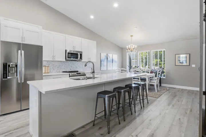 Contemporary kitchen featuring white cabinetry, stainless steel appliances, a white tile backsplash, and light wood-finish flooring