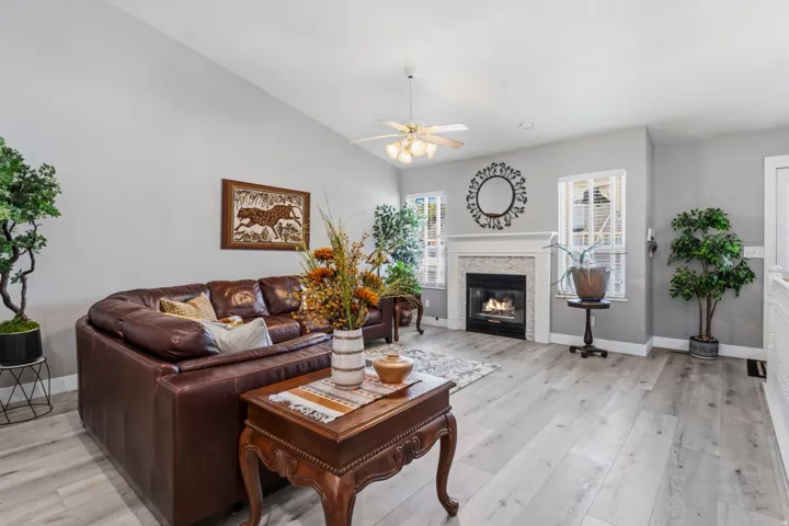 Vaulted ceiling, wood-finish flooring, white trim, recessed fireplace with tile surround, and an overhead ceiling fan