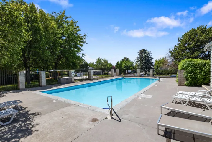 Outdoor swimming pool with concrete decking, surrounded by mature trees and a perimeter fence with brick pillars
