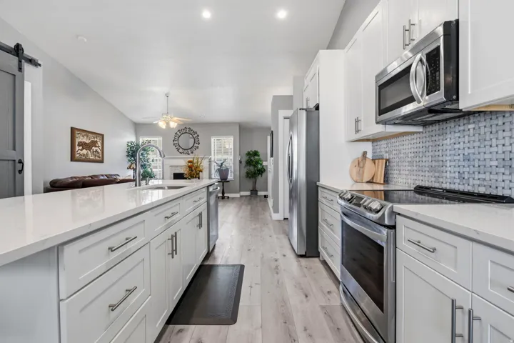 Modern kitchen with stainless steel appliances, white cabinetry, a tile backsplash, and light wood-finish flooring