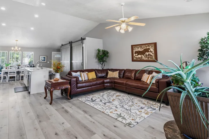 Vaulted ceiling, ceiling fan with integrated lighting, recessed lighting, wood-finish flooring, and barn doors