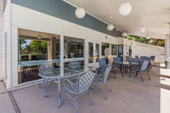 Covered patio area between Clubhouse and Pool featuring concrete flooring, multiple globe pendant lights, and a brick accent wall
