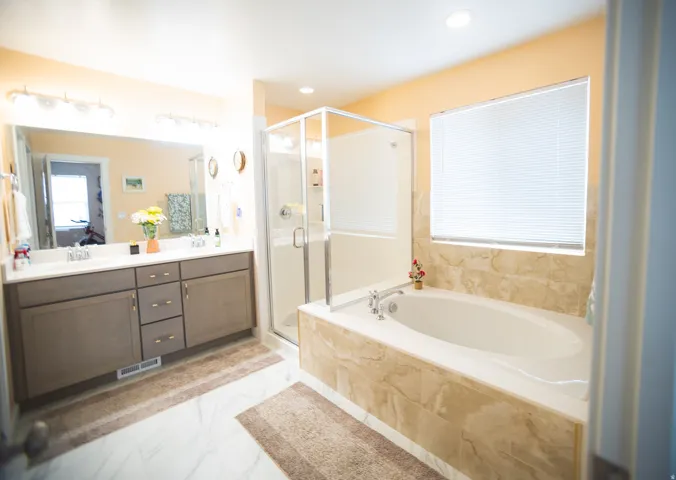 Dual vanity with undermount sinks, separate soaking tub with tiled surround, and glass-enclosed shower