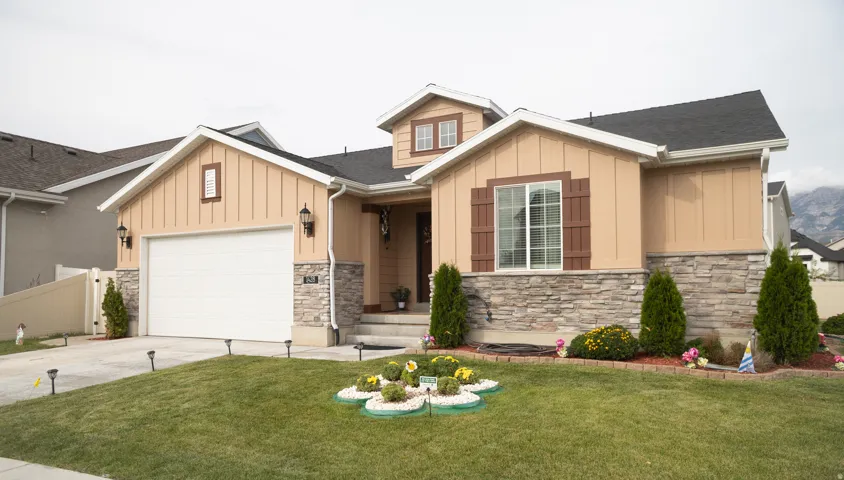 Single-family residence featuring a two-car garage, stone and board-and-batten siding, a prominent front window with decorative shutters, and established front landscaping