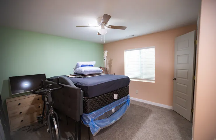 Neutral tone wall finishes, carpeting, ceiling fan with integrated lighting, and a window with blinds