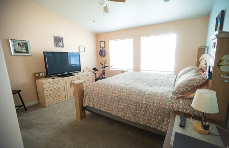 Vaulted ceiling with a ceiling fan, carpeted flooring, and two windows