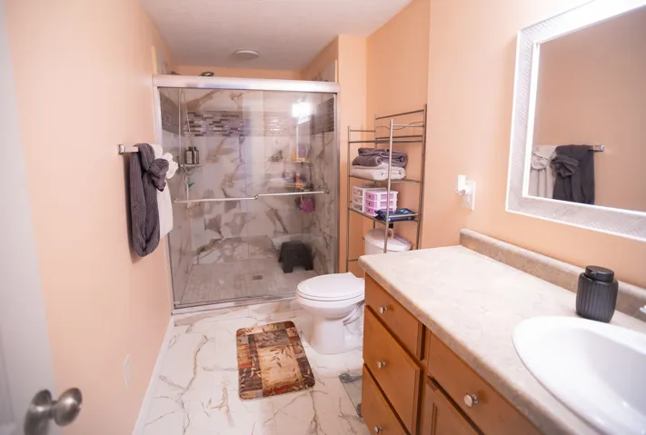 Walk-in shower with glass enclosure, vanity with integrated sink, wood-finish cabinetry, and white-framed mirror