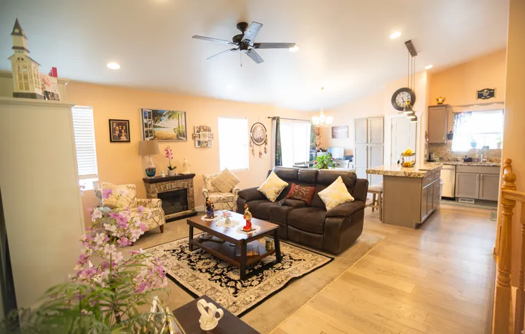 Open-concept living space featuring wood-finish flooring, a stone-surround fireplace, and an integrated kitchen island with a light-colored countertop
