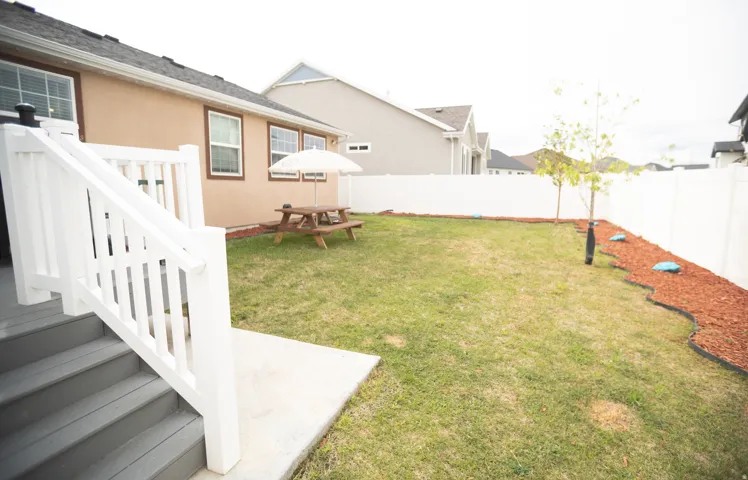 Private backyard featuring a white vinyl fence, wood chip landscaping, and a concrete patio