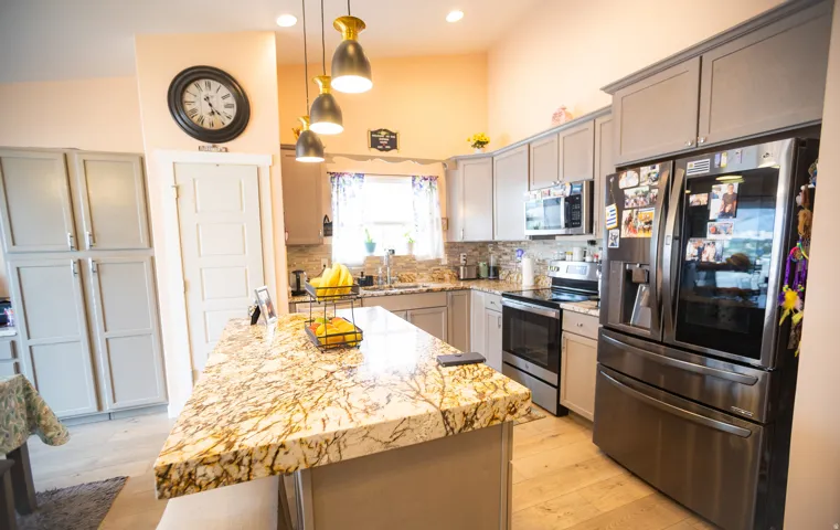 Vaulted ceiling kitchen featuring a large island with a patterned countertop, gray cabinetry, stainless steel appliances, and wood-finish flooring