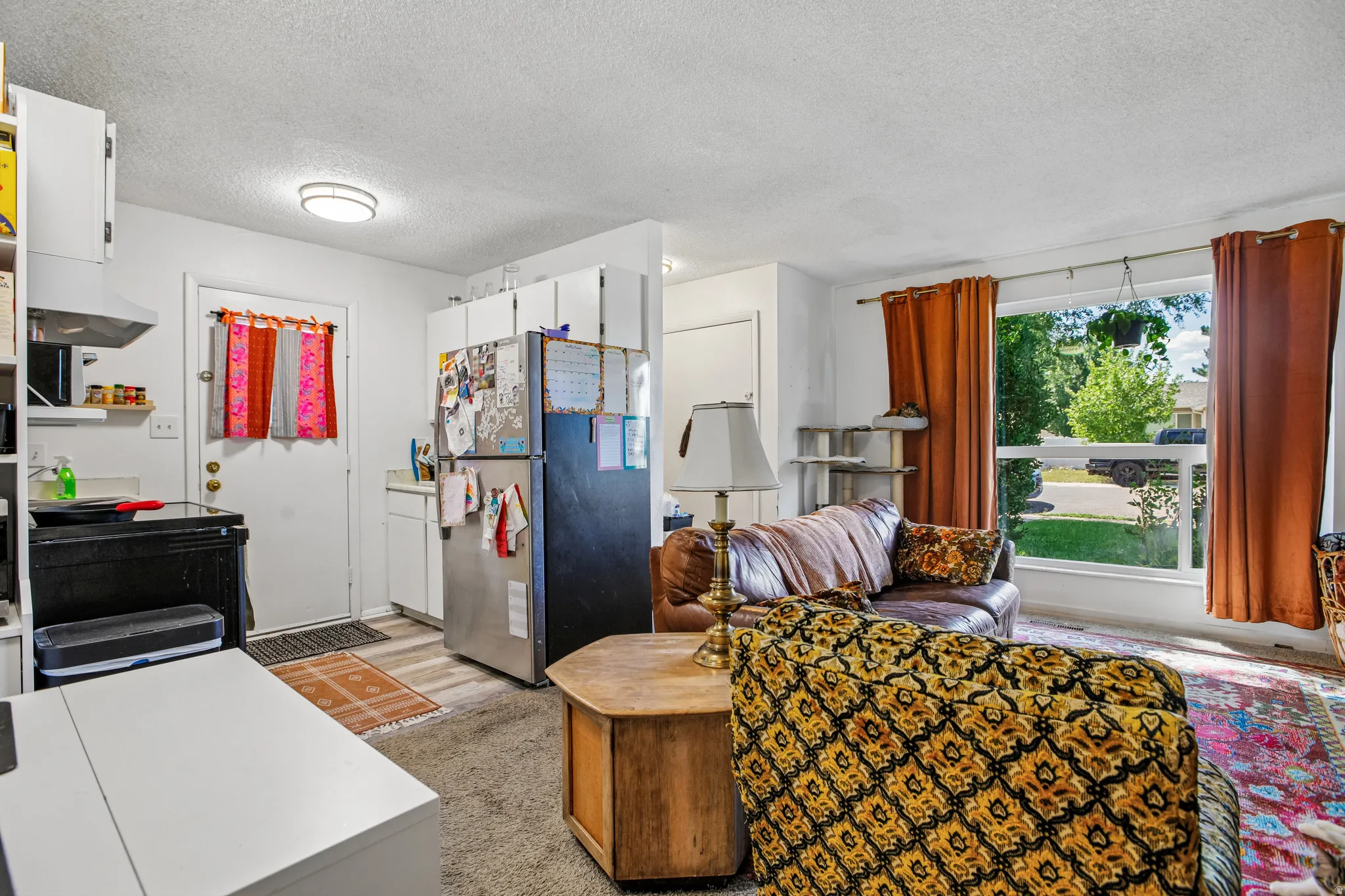 Open concept living area with a large picture window, kitchen with white cabinetry, stainless steel refrigerator, and wood-finish flooring