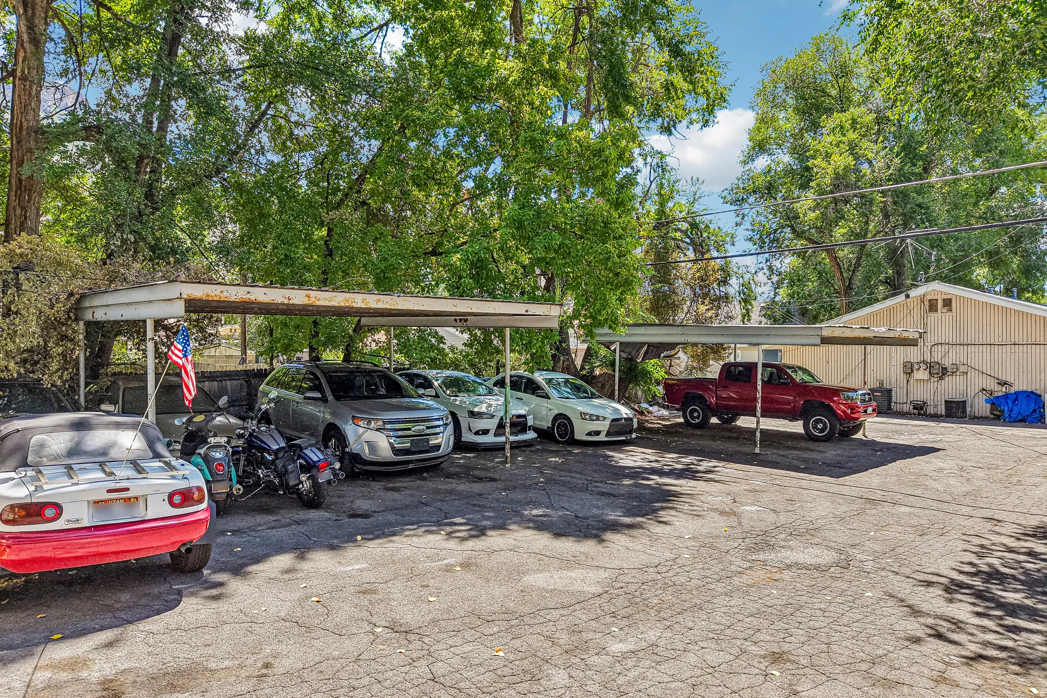 Expansive paved parking area featuring multiple carport structures and mature trees