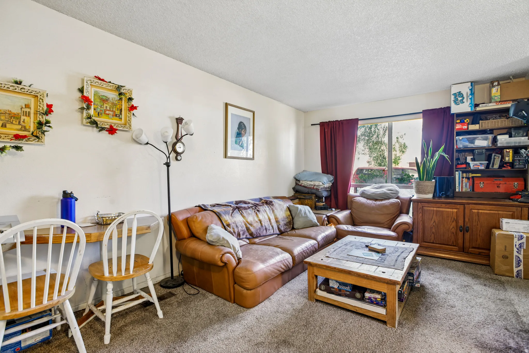 Carpeted living area featuring a large window with privacy drapes and a built-in wood-finish storage cabinet