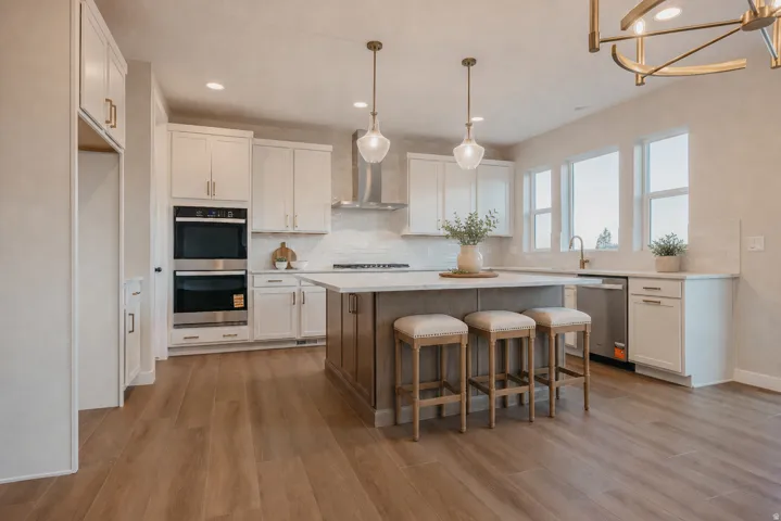 Spacious kitchen featuring wood-finish flooring, an oversized island, stainless steel double ovens, a stainless steel range hood, and white cabinetry