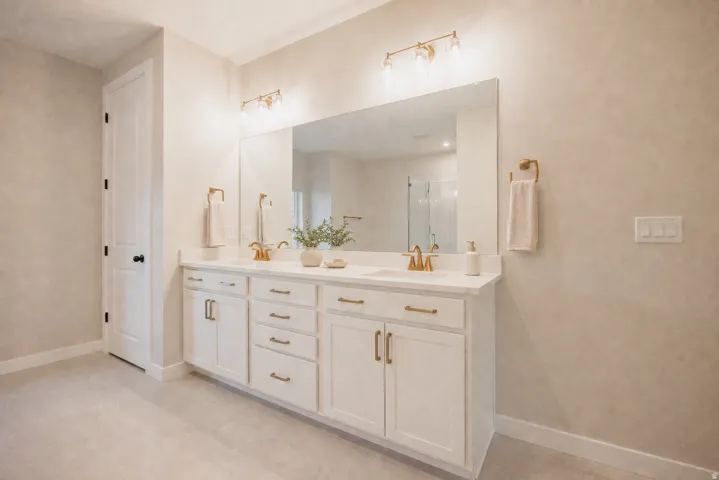 Dual vanity with white cabinetry, gold-finish hardware, and a single large mirror