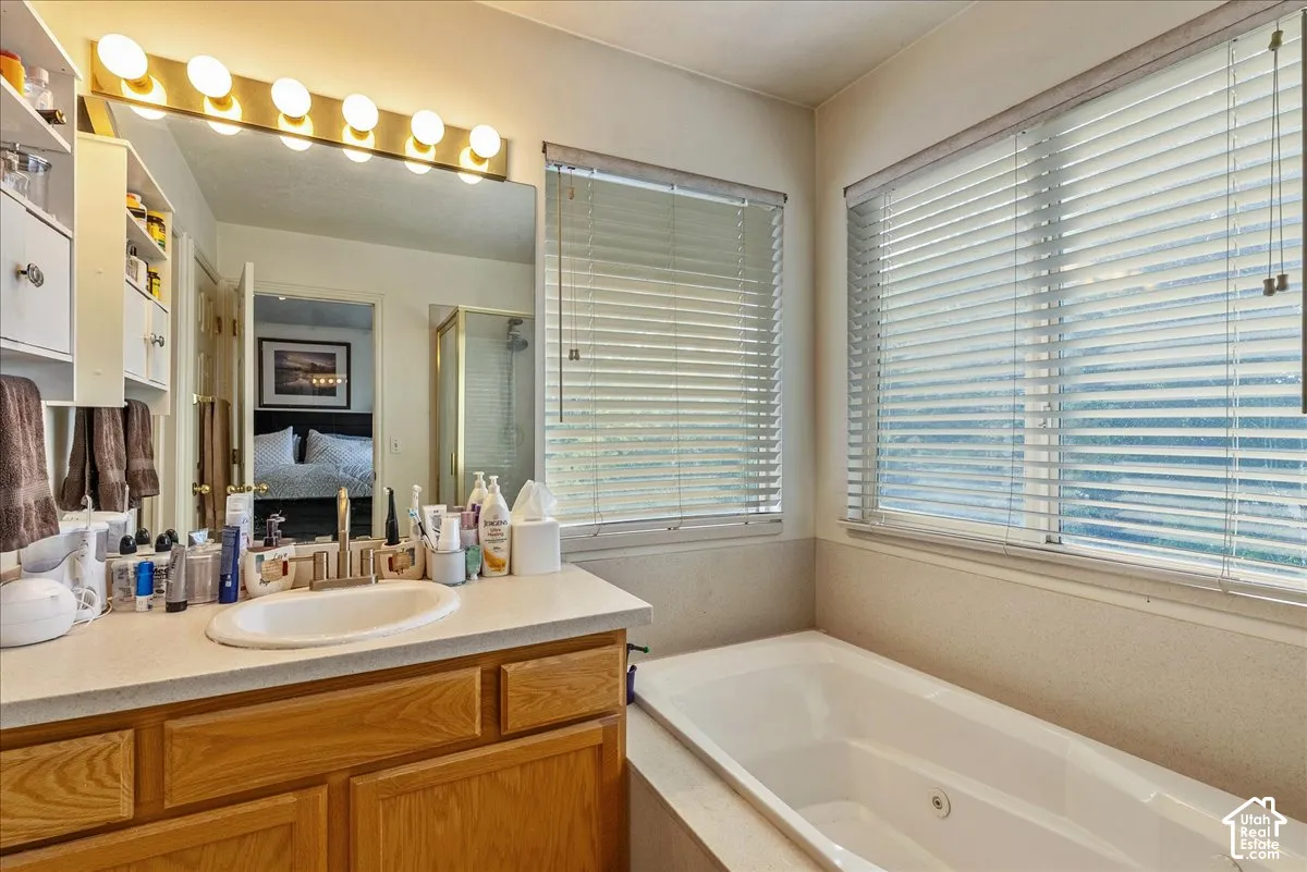 Bathroom featuring a built-in soaking tub, a vanity with wood-finish cabinetry, and a large mirror with integrated lighting