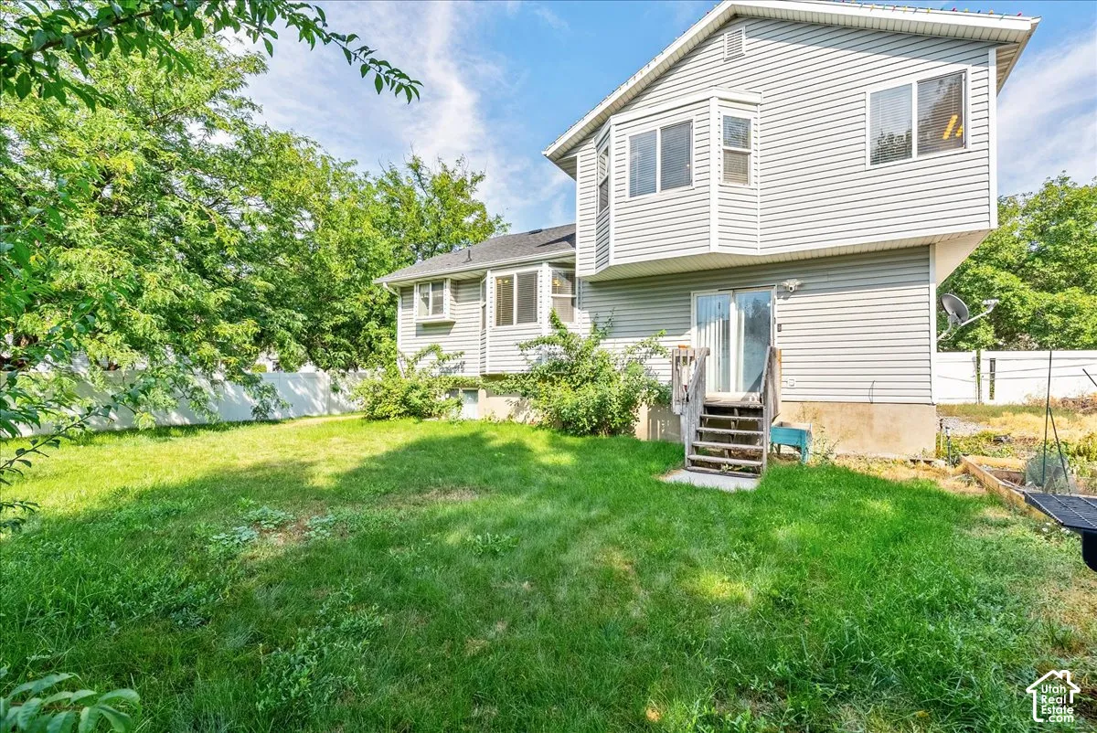 Expansive green lawn, white privacy fence, mature trees, multi-level siding exterior, and sliding glass door with wood steps
