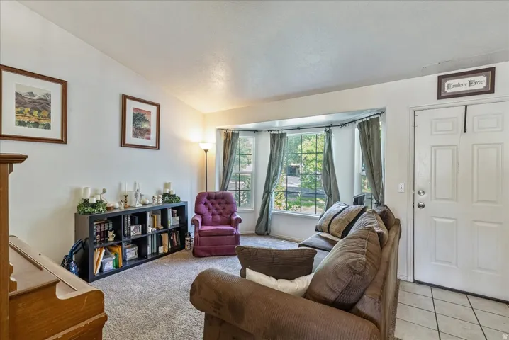 Bright living room with large multi-pane windows, neutral wall-to-wall carpeting, tile flooring at entry, built-in shelving unit with storage, and recessed ceiling lighting
