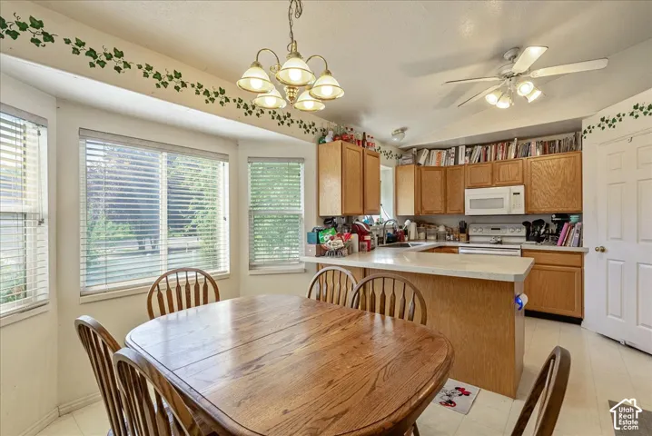 Kitchen with bay window, wood-finish cabinetry, white appliances, ceiling fan, and pendant lighting
