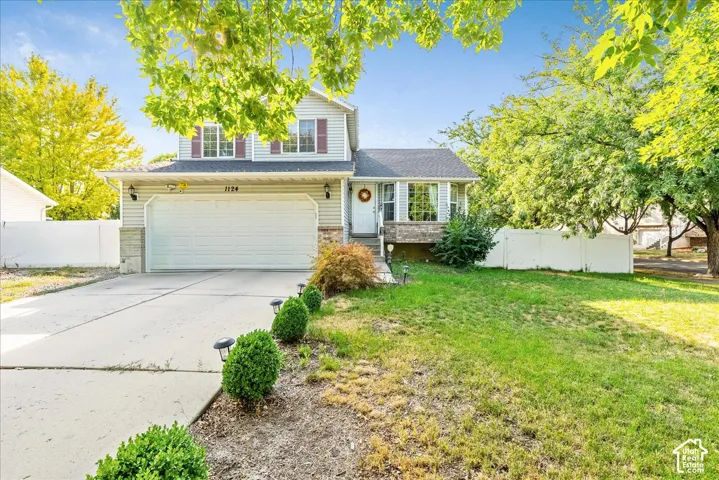 Two-story residence featuring light siding, a two-car garage with a concrete driveway, and a front lawn with established landscaping