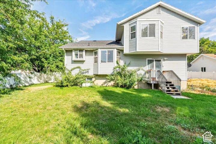 Wood deck with stairs, light-toned siding, bay window, white fencing, and a grassy yard
