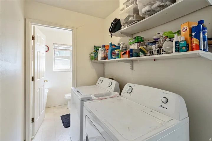 Laundry area with white appliances, open shelving, and a nearby white door leading to a bathroom with a window