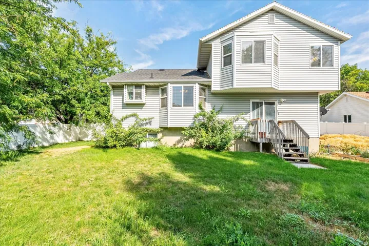 Wood deck with stairs, light-toned siding, bay window, white fencing, and a grassy yard