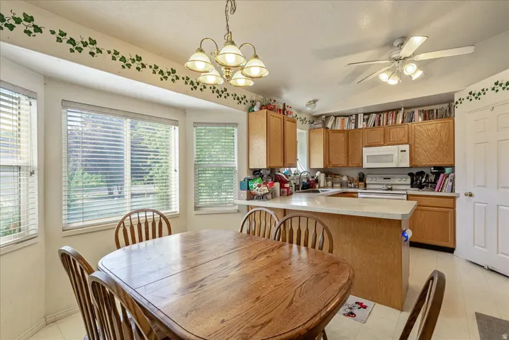 Kitchen with bay window, wood-finish cabinetry, white appliances, ceiling fan, and pendant lighting