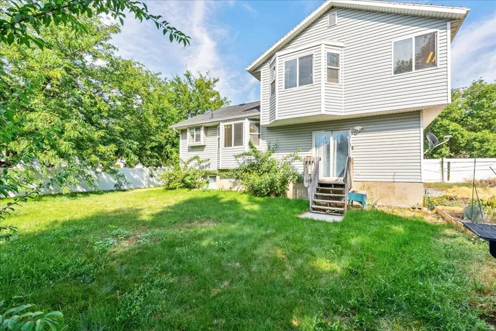 Expansive green lawn, white privacy fence, mature trees, multi-level siding exterior, and sliding glass door with wood steps