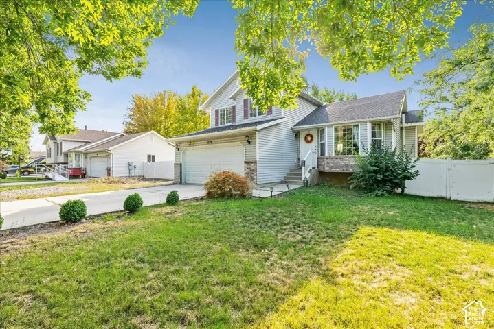 Two-story residence featuring siding exterior, an attached garage, a concrete driveway, and a front yard with mature landscaping