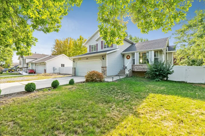 Two-story residence featuring siding exterior, an attached garage, a concrete driveway, and a front yard with mature landscaping