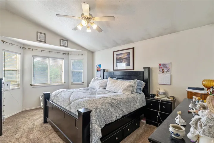 Vaulted ceiling with a ceiling fan, carpet flooring, and a bay window