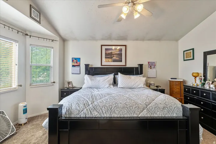 Carpeted bedroom featuring a vaulted ceiling with a ceiling fan, dual windows with blinds, and a built-in wall niche