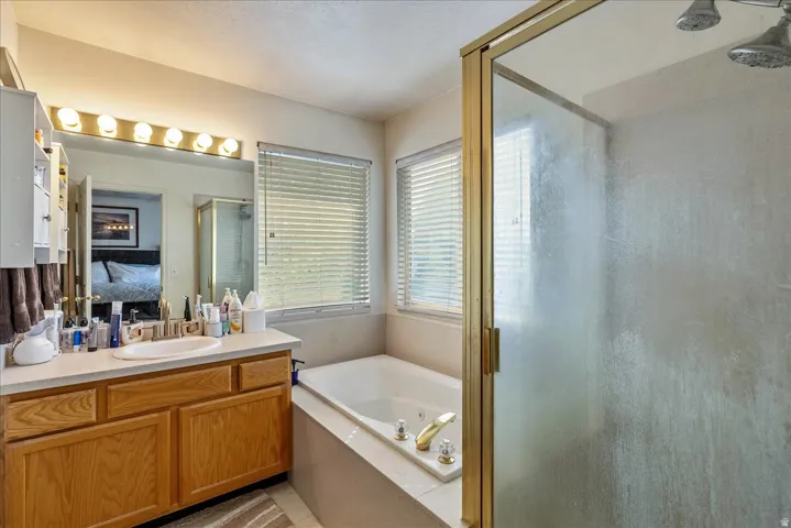 Dual vanity with wood-finish cabinetry, built-in soaking tub, and a shower with a gold-tone framed glass enclosure
