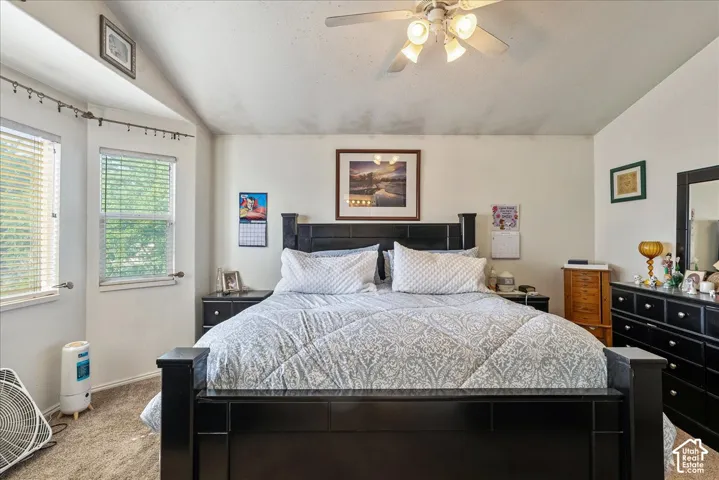 Carpeted bedroom featuring a vaulted ceiling with a ceiling fan, dual windows with blinds, and a built-in wall niche